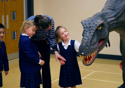 Children smiling and interacting with a large scale 'dinosaur'