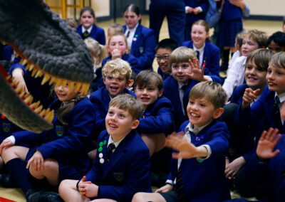 A group of children sat smiling with a fake dinosaur infront of them
